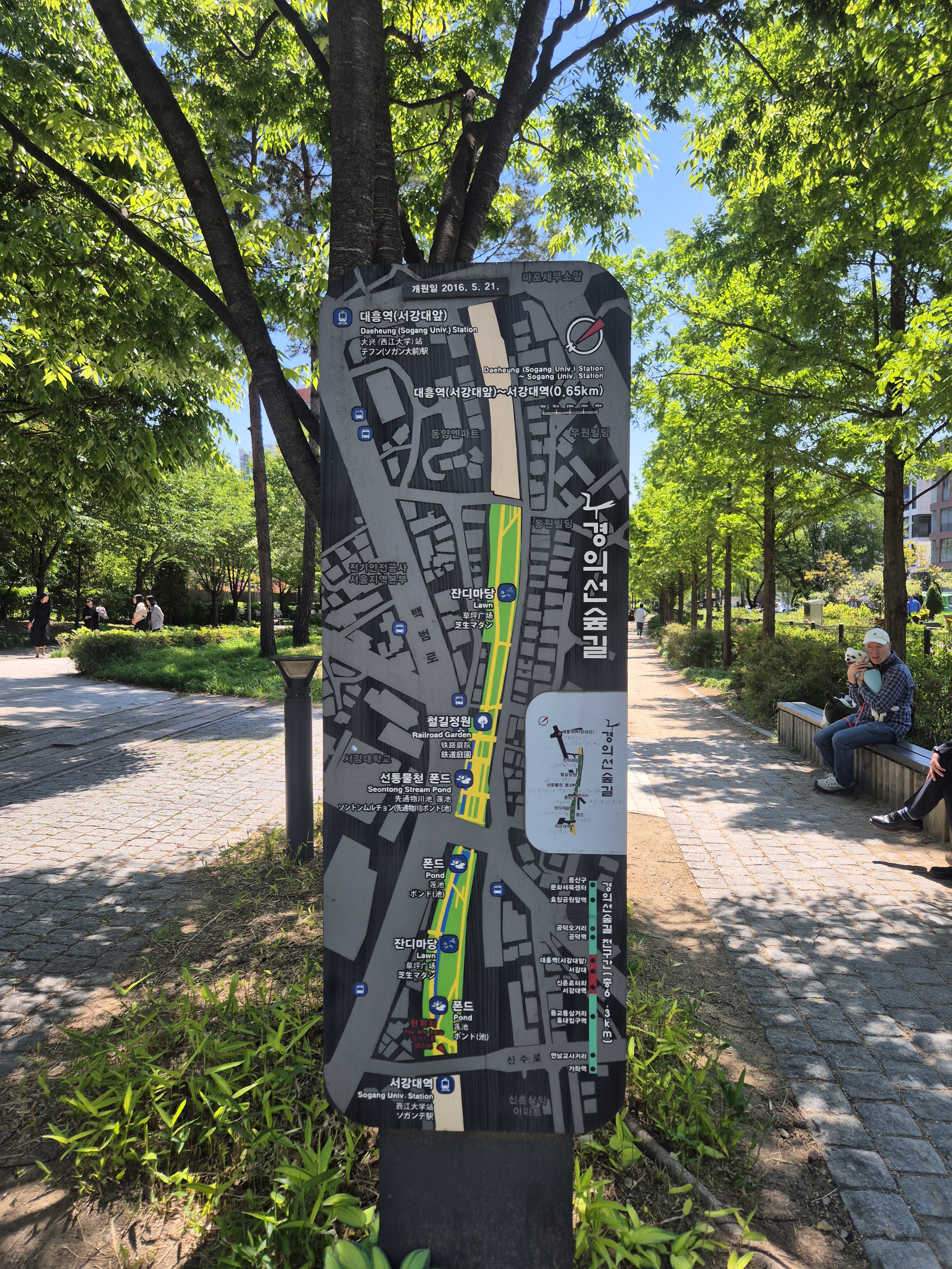 A detailed map in a park showing nearby attractions and routes, with labels in multiple languages, surrounded by greenery on a sunny day.