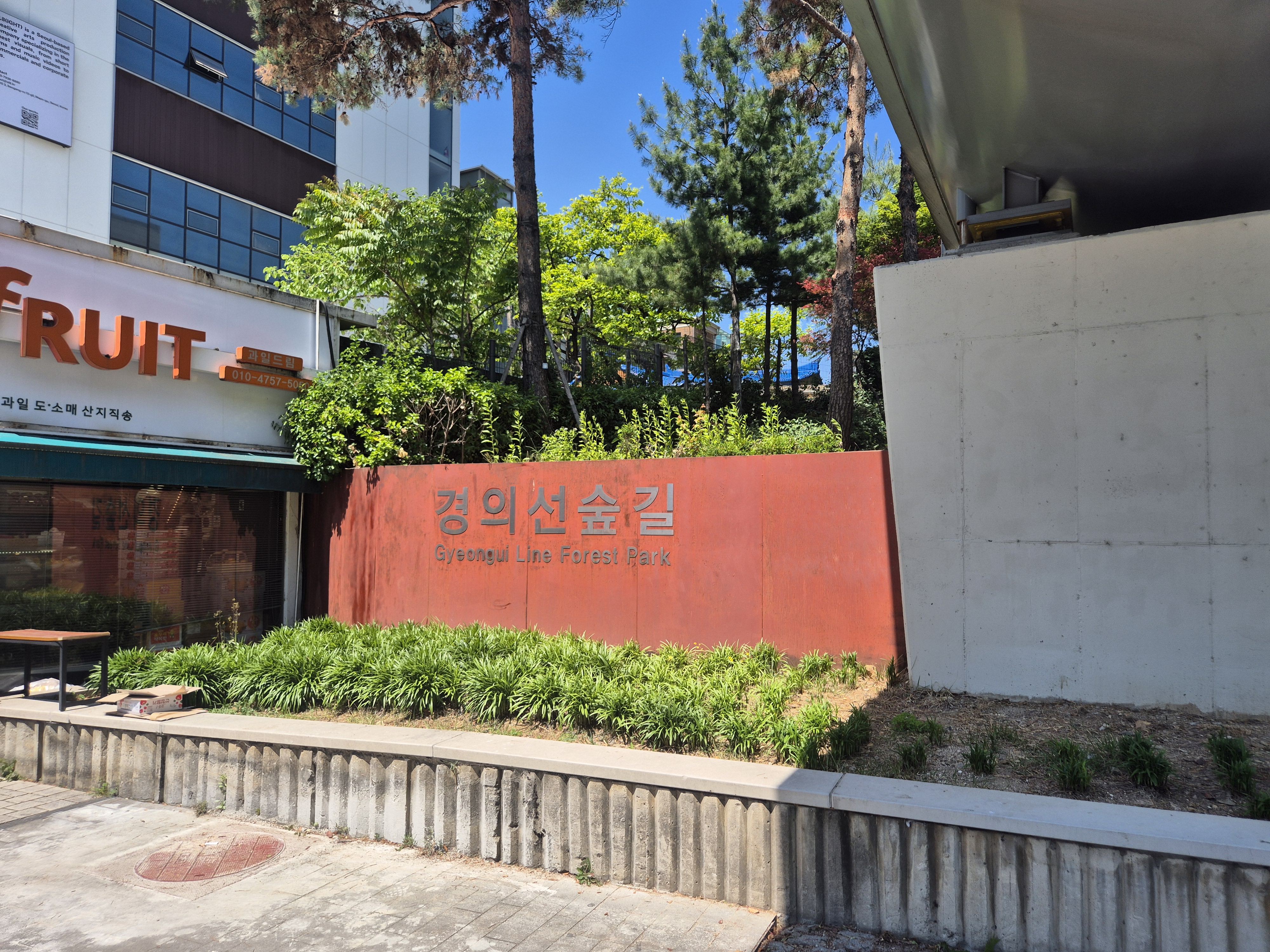 Sign for Gyeongui Line Forest Park displayed in front of green foliage and a building.